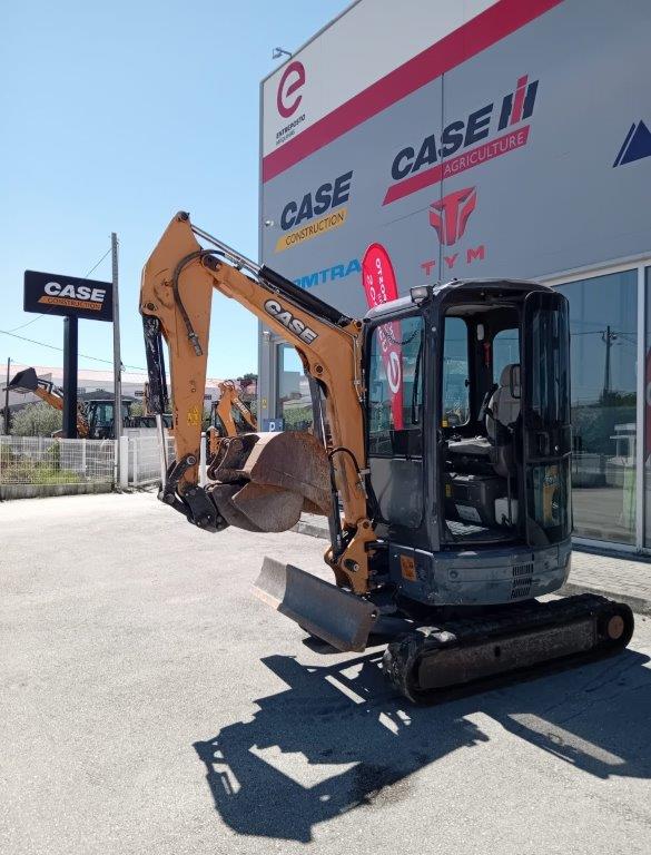 Uma Mini Giratória CASE CX26B parada em frente a um edifício de uma empresa.